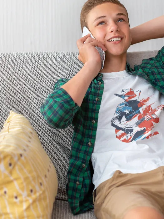 Teenage boy wearing a Western-themed T-shirt with cowboy guitarist and American flag graphic – youth apparel by Rugged Rhythm.